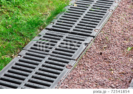 iron grate of a drainage channel on a landscape with pebbles and green grass, closeup detail. 72541854