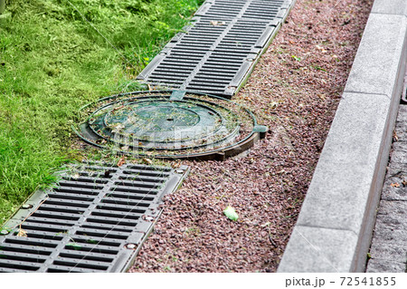 round manhole cover of drainage system on the side of the road with an iron grate and pebbles. round manhole cover of drainage system on the side of the road with an iron grate and pebbles. 72541855