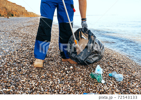 Close up photo of a man collecting garbage with a grabbing tool on the beach 72543133