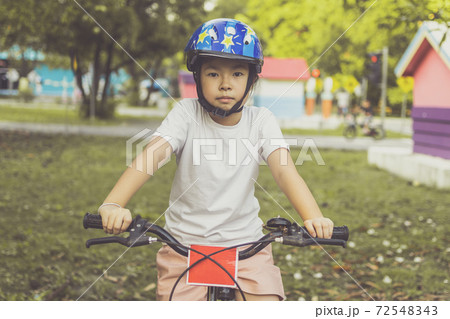 Asian girl learns to ride bike in park. Portrait of a cute kid on bicycle. 72548343