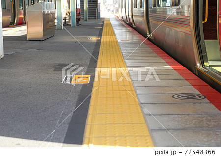 駅のプラットホーム　黄色い点状ブロックと停車中の列車 72548366