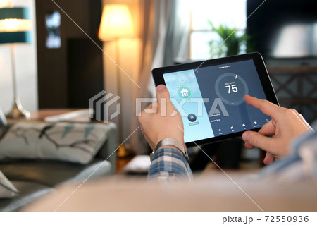 Man is Adjusting a temperature using a tablet with smart home app in modern living room 72550936
