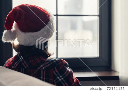 Back view of lonely european young woman wrapped in a plaid with with alarm clock sitting near window at cold winter day. Back view of lonely european young woman wrapped in a plaid with with alarm clock sitting near window at cold winter day. 72551125