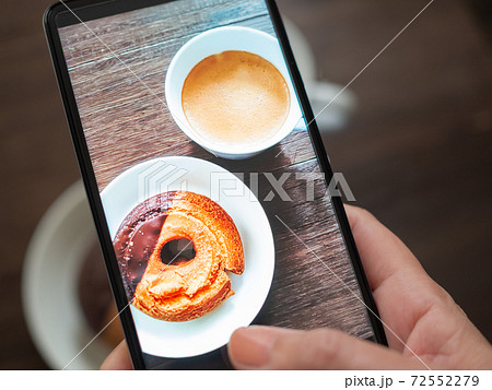 テーブルの上のドーナツをスマートフォンで撮影する女性の手 72552279