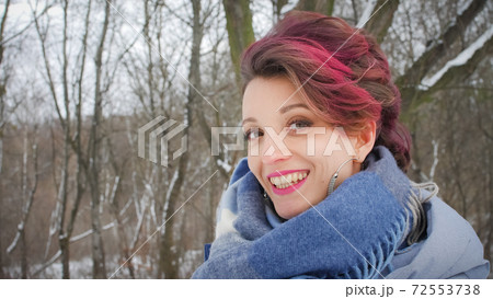 Attractive young woman with perfect skin and makeup with dark pink hair is possing on winter park background wearing blue scarf and silver earrings Attractive young woman with perfect skin and makeup with dark pink hair is possing on winter park background wearing blue scarf and silver earrings 72553738