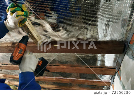 The wizard uses a cordless drill and screw the screws into boards that hold foil film and mineral wool to heal the roof of the house The wizard uses a cordless drill and screw the screws into boards that hold foil film and mineral wool to heal the roof of the house 72556280