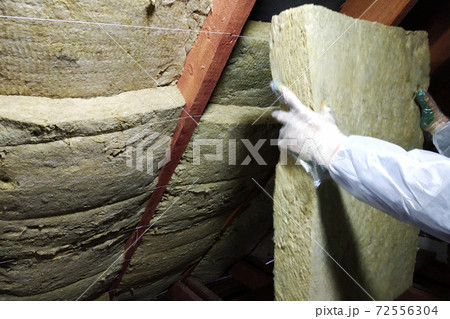 A man in a protective overalls puts mineral wool between the beam of the roof of the house for his warming from the cold 72556304