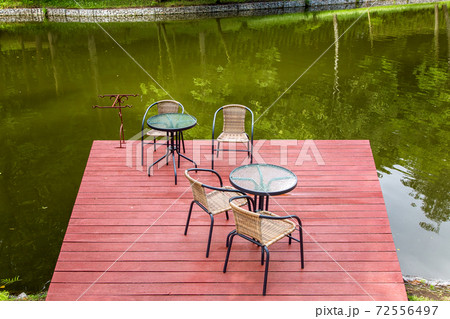 outdoor river cafe with tables and chairs on a wooden red pier on the pond, empty chairs nobody. outdoor river cafe with tables and chairs on a wooden red pier on the pond, empty chairs nobody. 72556497