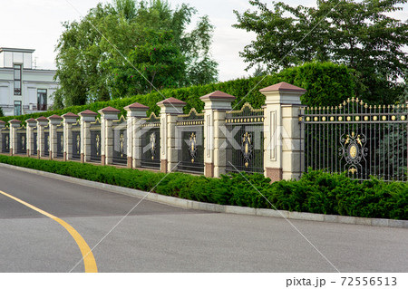 a stone fence with a rustik and an iron forged insert with a pattern and peaks near asphalt road along the fence. a stone fence with a rustik and an iron forged insert with a pattern and peaks near asphalt road along the fence. 72556513