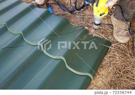 The master drill a hole with a professional drill sheet of metal for mounting on the roof of the house 72556744