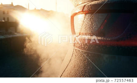 Tail light of a frosted car and polluting exhaust smoke on orange sunny background 72557463