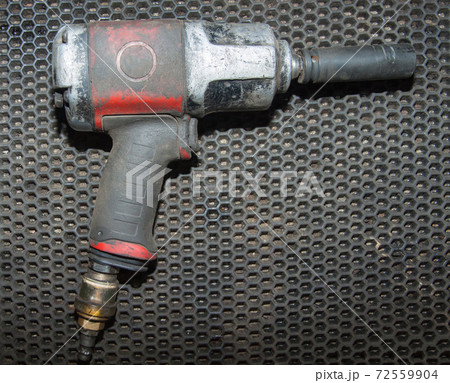 An old dirty pneumatic wrench is lying on the workbench of an auto repair shop 72559904