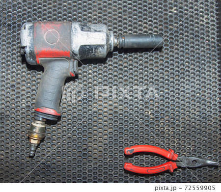 A dirty old pneumatic wrench and red pliers lie on the workbench of an auto repair shop. Close-up 72559905