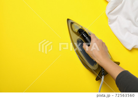 Female hand hold modern iron on yellow background, top view Female hand hold modern iron on yellow background, top view 72563560
