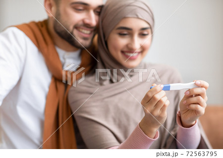 Joyful Muslim Couple Holding Pregnancy Test Sitting Together Indoors 72563795