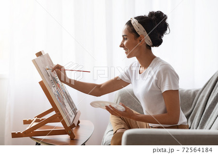 Side view of young woman sitting on couch and painting 72564184