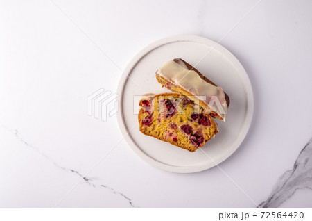 Two pieces of cupcake with cranberries and icing sugar on a white plate on a light background Two pieces of cupcake with cranberries and icing sugar on a white plate on a light background 72564420