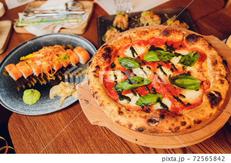 Thin-crust pizza topped with fresh basil leaves. Slices of pizza. Home made food. Italian vegetarian pizza. Concept for a tasty and hearty meal. Rustic wooden background. Thin-crust pizza topped with fresh basil leaves. Slices of pizza. Home made food. Italian vegetarian pizza. Concept for a tasty and hearty meal. Rustic wooden background. 72565842