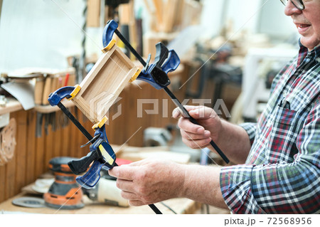 Senior carpenter glueing wooden craft surface and joining with clamps. Woodwork carpenter with equipment and tools at workshop. Handmade diy furniture.Wood part glue joiner 72568956