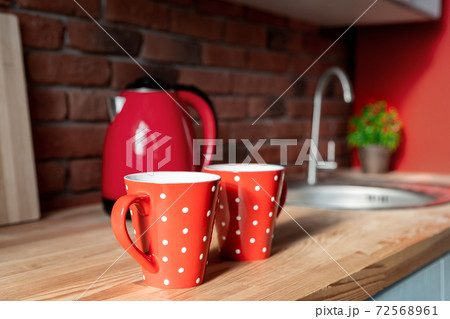 Pair Red polka dot retro vintage coffe tea mugs on wooden kithen counter at rustic room interior on breakfast time. Two hot drink cups and red kettle against brick wall decor design in cozy apartment 72568961