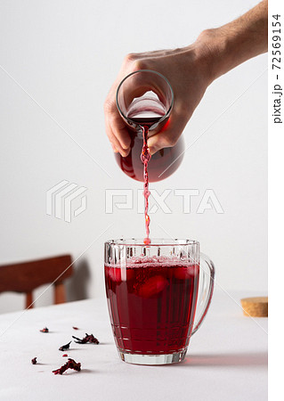 Man pours refreshing hibiscus tea into a glass with ice 72569154