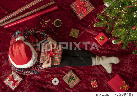 Top view of woman with christmas gift box on knees. Female wrapping gifts for family sitting on fluffy plaid near christmas tree. Flat lay. Top view of woman with christmas gift box on knees. Female wrapping gifts for family sitting on fluffy plaid near christmas tree. Flat lay. 72569485