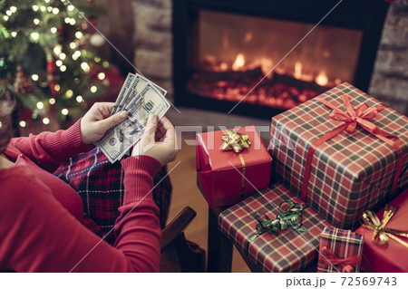 Christmas. Woman in sweater using tablet for searching gift ideas sitting at table near fireplace and christmas tree. Christmas. Woman in sweater using tablet for searching gift ideas sitting at table near fireplace and christmas tree. 72569743