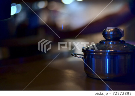 A steel pan with a closed lid on the table stands alone against a backdrop of light bokeh in a catering restaurant. 72572895
