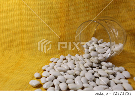 White dry beans in a jar lies spilled out on a yellow lemon background with a copy of the space 72573755