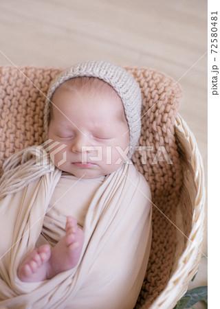 Cute little baby in a knitted hat with a toy bunny lies in a wicker basket decorated with greens and lemons in a beige knitted blanket. Summer mood. Happy healthy childhood 72580481
