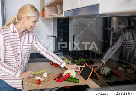 Woman standing in the kitchen and having a culinary video workshop Woman standing in the kitchen and having a culinary video workshop 72582367