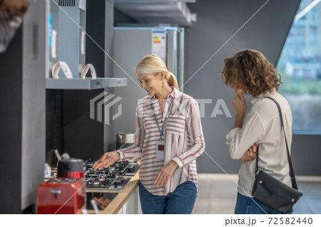 Sales assistant in striped shirt showing goods to the female customer 72582440