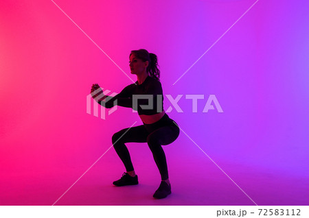 Full length portrait of a young fitness woman doing squatting isolated on a vibrant colors background 72583112
