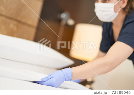 Young maid in gloves making bed in hotel room light Young maid in gloves making bed in hotel room light 72589040