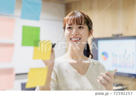 会議室で透明ボードにカラー付箋紙を貼る女性 72592257