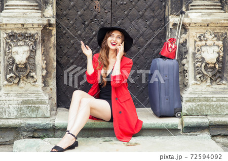 Smiling woman with a suitcase is talking by smartphone on stairs near old door. Smiling woman with a suitcase is talking by smartphone on stairs near old door. 72594092