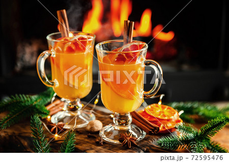 Mulled cider glasses on the background of fireplace fire. Hot mulled spiced apple cider cocktail for winter or autumn time. 72595476