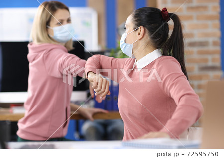 Two women in office in protective medical masks greet safely Two women in office in protective medical masks greet safely 72595750