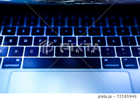 青く光るノートパソコンのキーボードのイメージの写真素材