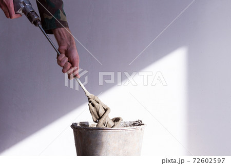 stirrer in the hand of a worker in a cement mortar and an old rusty bucket close up stirrer in the hand of a worker in a cement mortar and an old rusty bucket close up 72602597