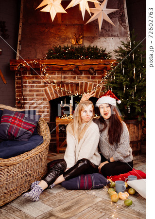 Two woman by fireplace with New Year's decoration. Romantic relationships. Two woman by fireplace with New Year's decoration. Romantic relationships. 72602763