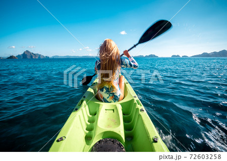 Woman paddling a kayak at sea with distant mountains ahead Woman paddling a kayak at sea with distant mountains ahead 72603258