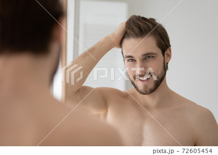 Happy shirtless confident young man styling hair with fingers. 72605454