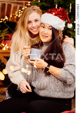 Two woman drinking tea by fireplace with New Year's decoration. Romantic. 72605963