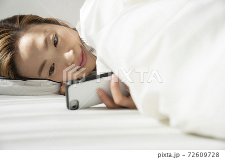 寝起きでスマートフォンを見る女性 寝起きでスマートフォンを見る女性 72609728