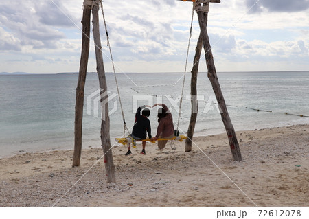 海辺のブランコに乗って 手でハートをつくる2人の写真素材