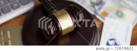 Wooden gavel for judge lies on table next to one hundred dollar bills and bank credit cards. Wooden gavel for judge lies on table next to one hundred dollar bills and bank credit cards. 72619921