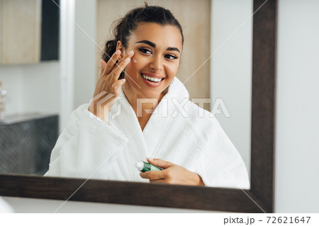 Middle east woman applying cream in bathroom mirror Middle east woman applying cream in bathroom mirror 72621647