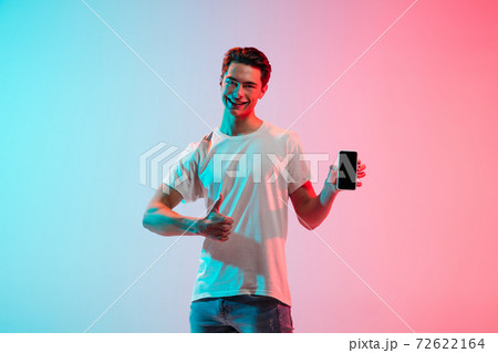 Young caucasian man's portrait on gradient blue-pink studio background in neon light 72622164