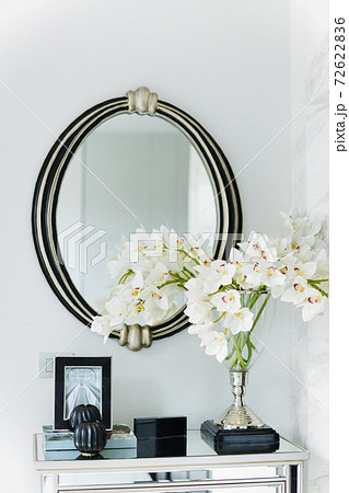Round Mirror on a wall above glass table with flowers in living room interior. 72622836